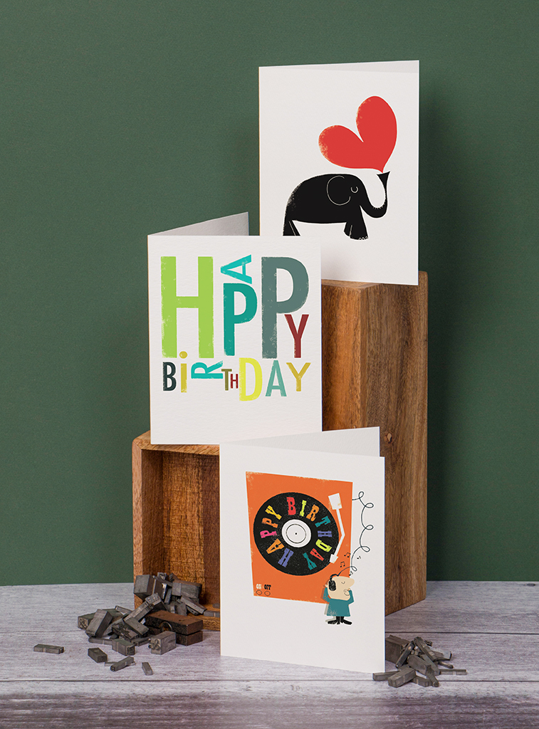Ink Press Mini Image of three brand new additions to the Ink Press Minis Range. Dark Green Background. First greetings card is a black elephant and a red heart, second card says 'Happy Birthday' in bright colours, third card is a cartoon man with his eyes closed listening to a huge orange record player. The record in the player says 'Happy Birthday' on it and there are little music notes around the man's head.